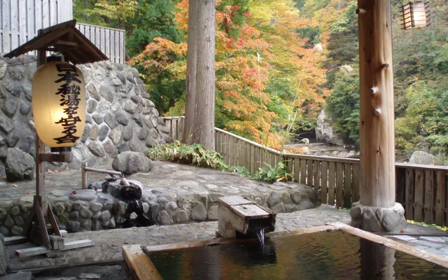 Un bain thermal en plein air en pierre, entouré d’arbres aux couleurs d’automne