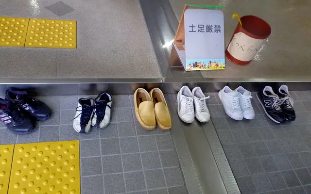 Des chaussures alignées à l’entrée d’un bâtiment japonais, sous un panneau demandant de les retirer
